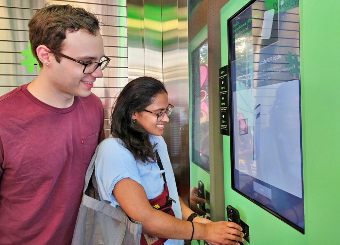 미국인 탄비(Tanvi, 오른쪽)씨와 러셀(Russell, 왼쪽)씨가 올리브영 명동 타운에 설치된 벤딩머신으로 글로벌몰에 가입하는 모습. 사진=CJ올리브영